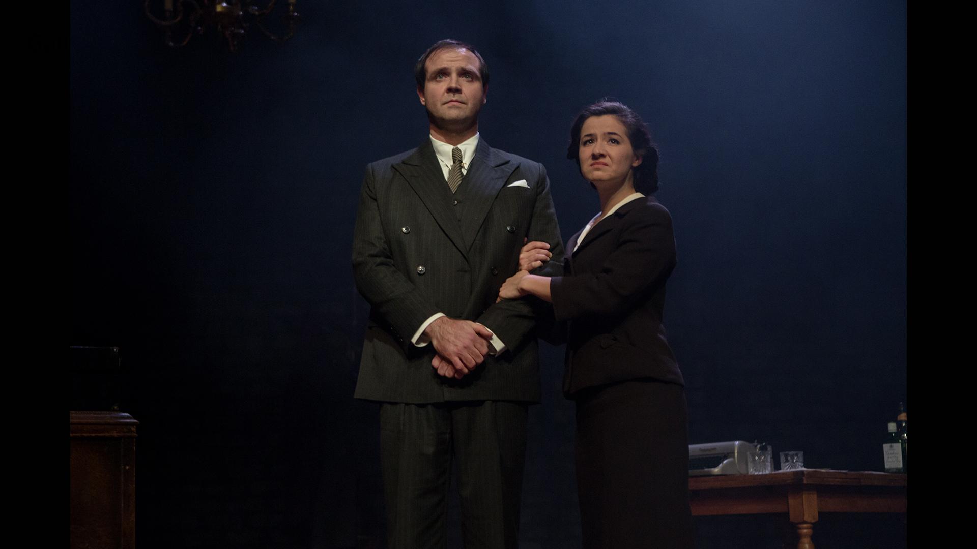 An actor depicting Nye Bevan dressed in a suit with an actor as Jennie Lee standing at his side holding his arm
