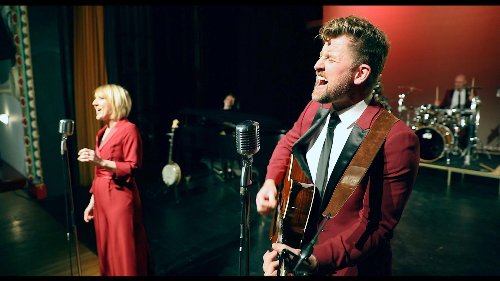 Two singers dressed in red, one playing a guitar