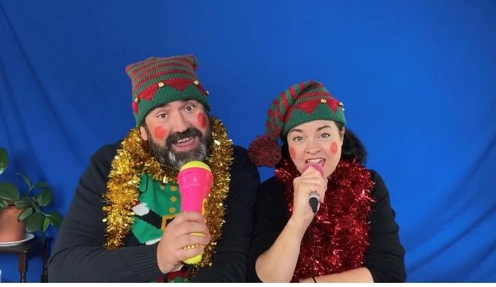 Photo of a couple dressed as elves with plastic microphones and wearing tinsel around their necks