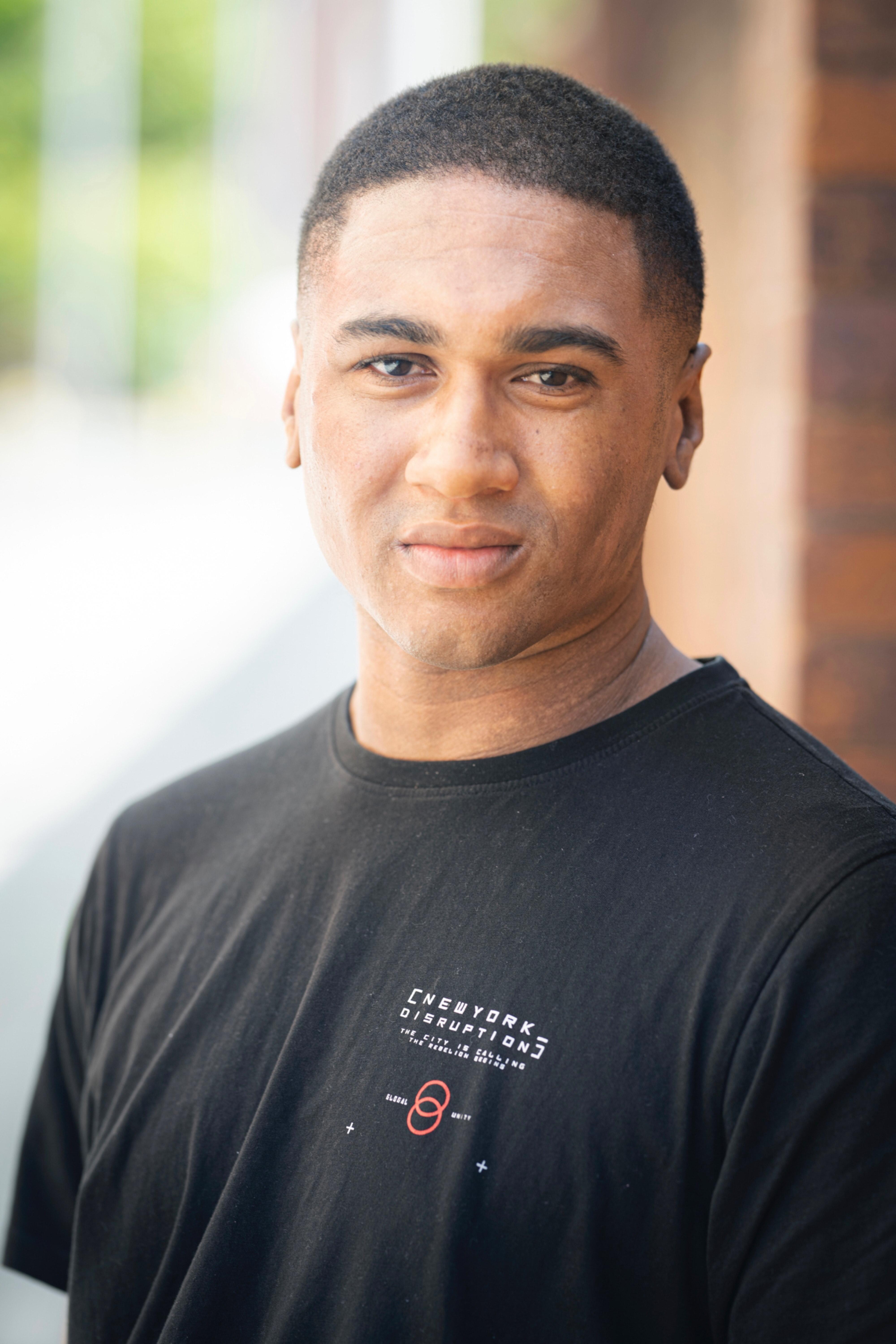 Black man with short black hair wearing a black t shirt