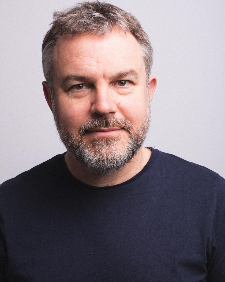 White man with greying hair and facial hair