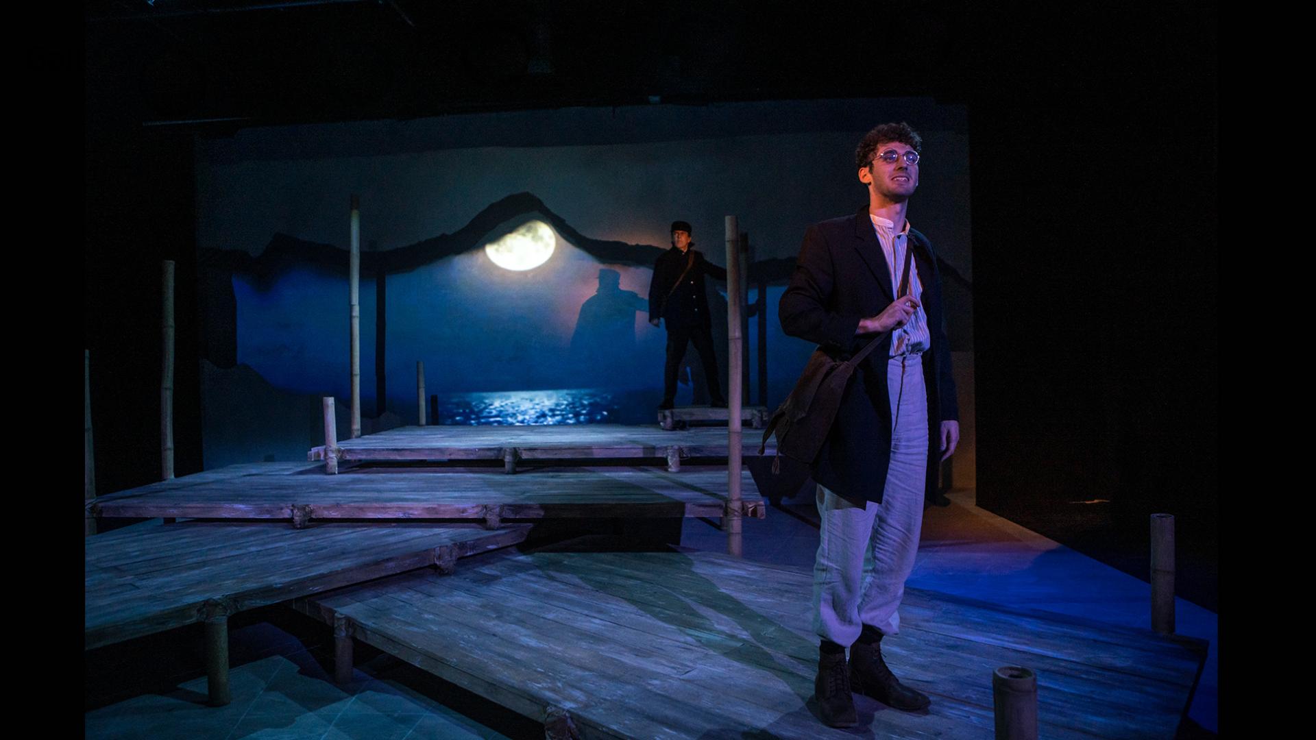 A man stands on a wooden deck with the moon in the background.