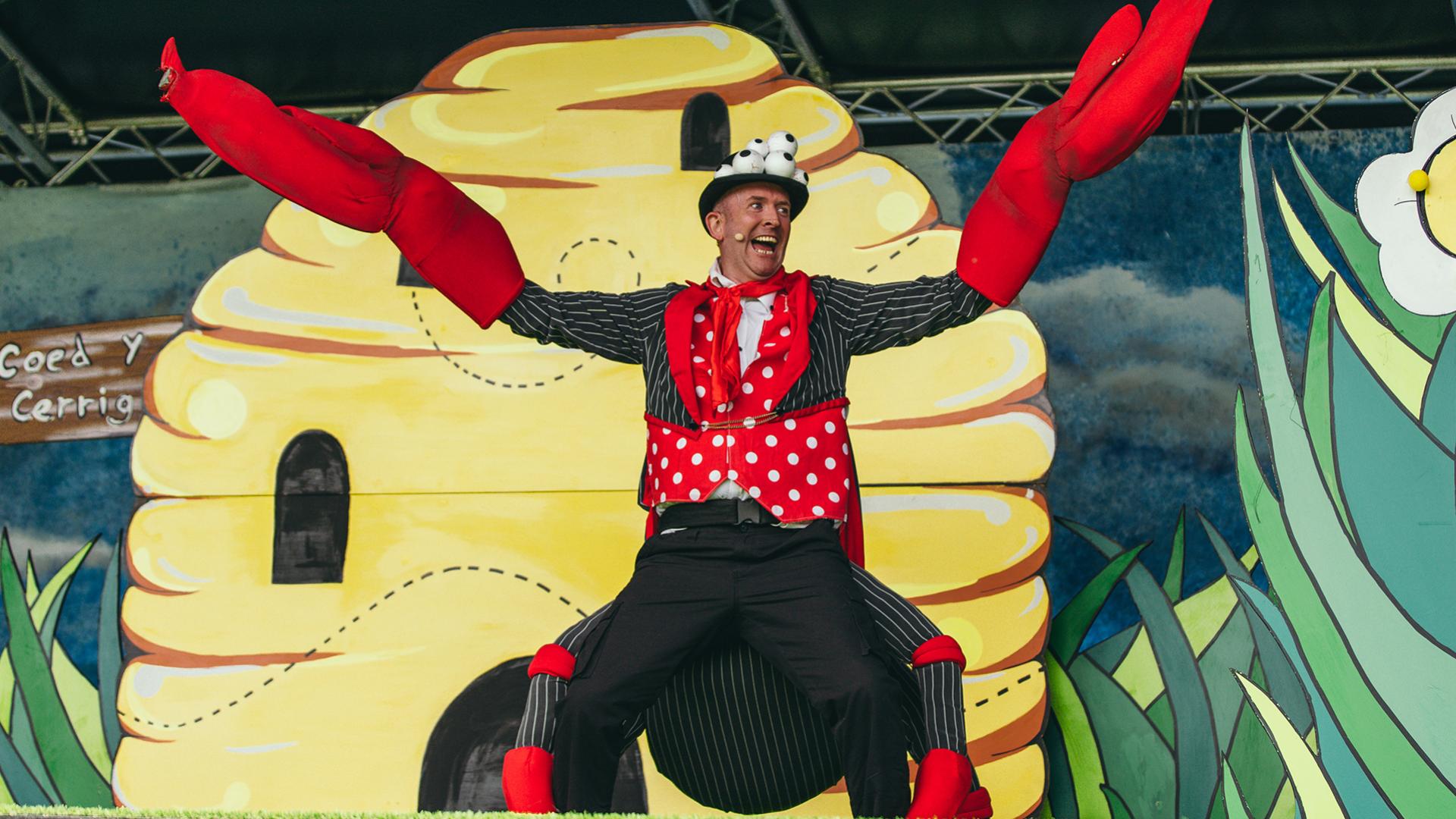 A man dressed as a crab spider standing in front of a stage set of a behive.