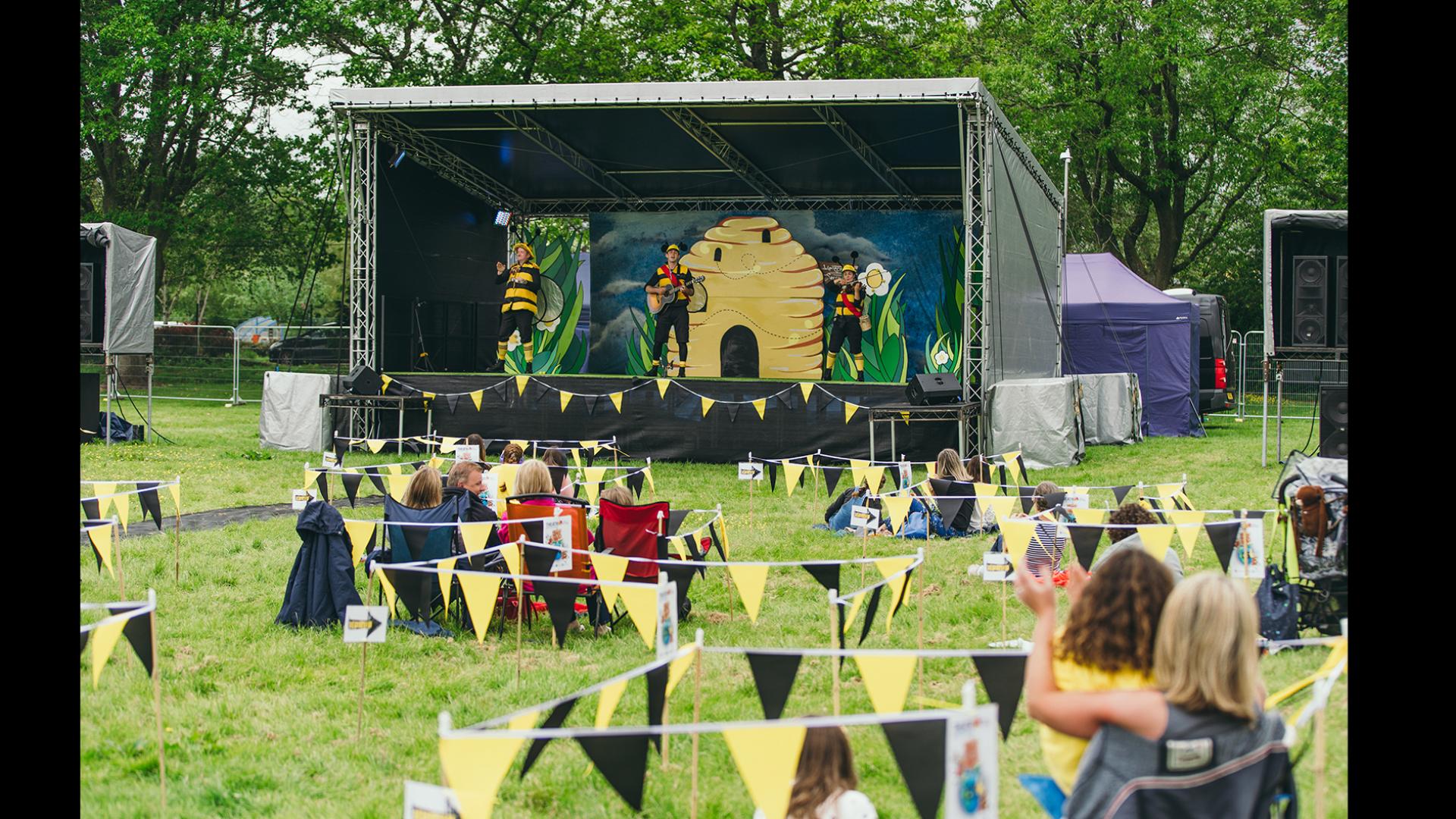 An outdoor stage with people sat on the grass watching.