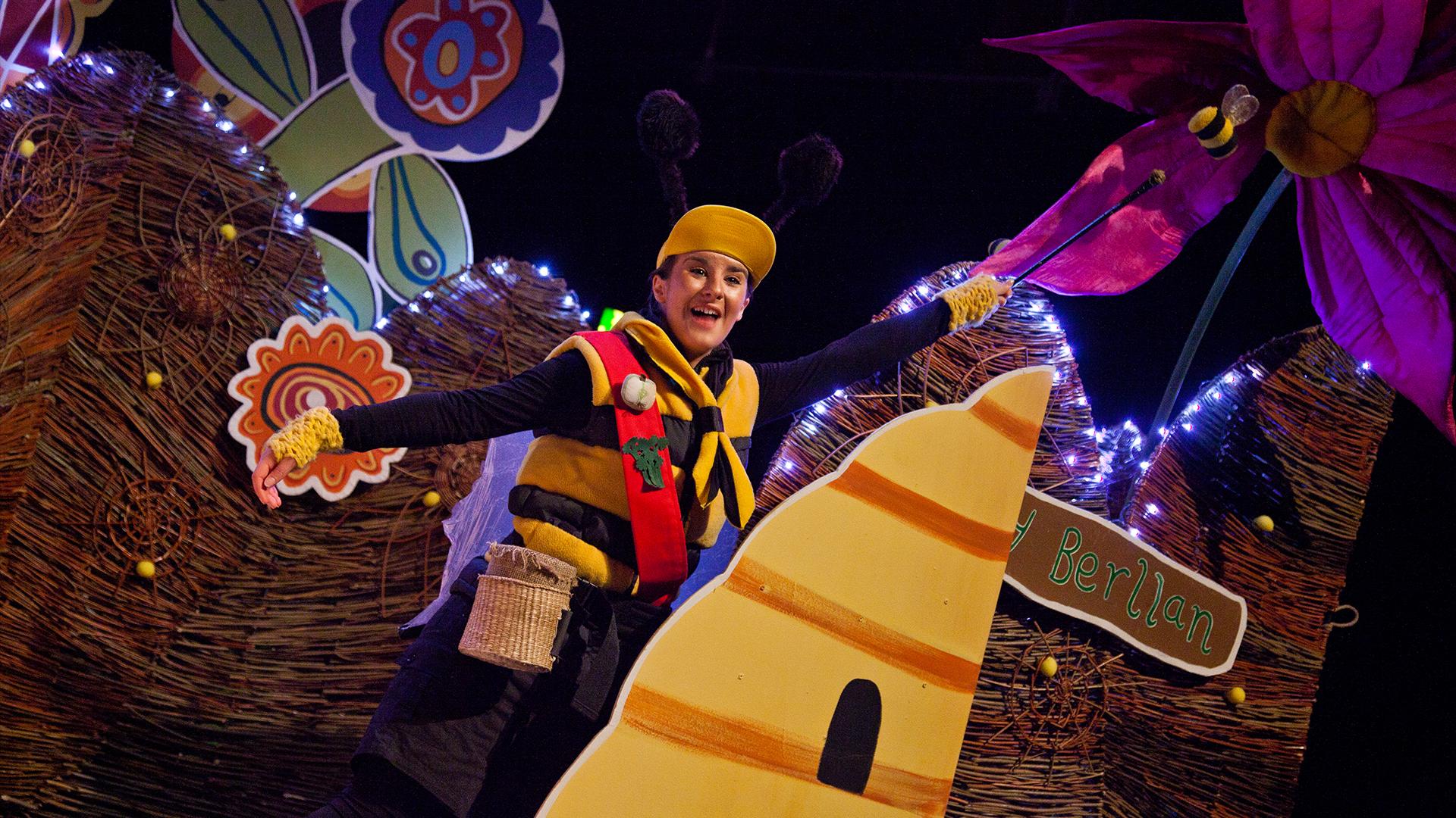 A woman dressed as a bee standing behind a stage set of a beehive