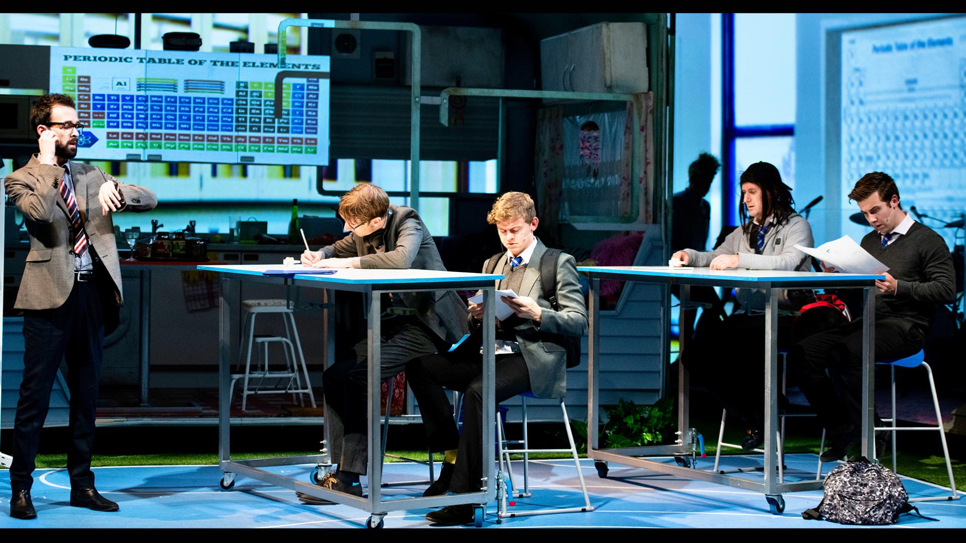 Classroom scene with four pupils sat at science tables and the teacher at the front of the class