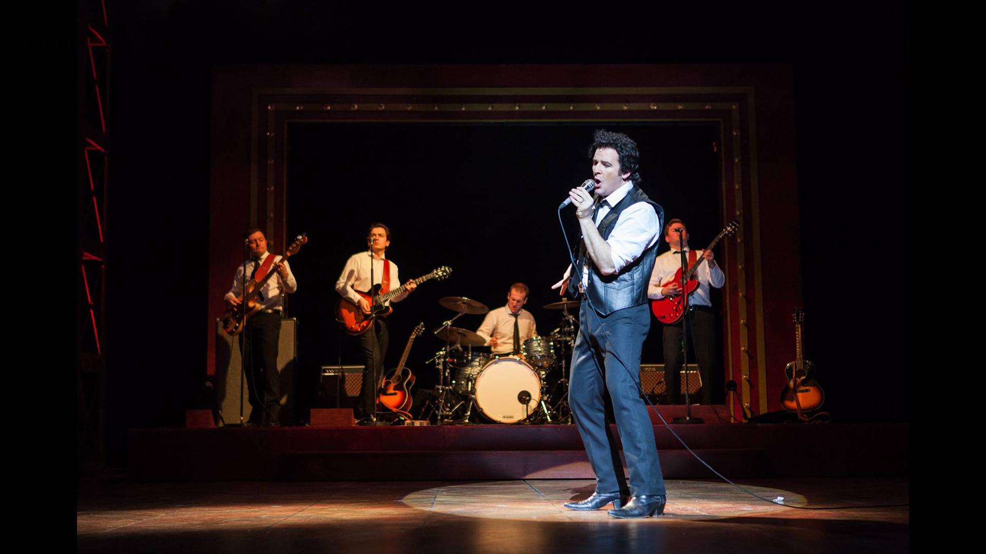 Actor dressed as Tom Jones singing on stage in front of a band