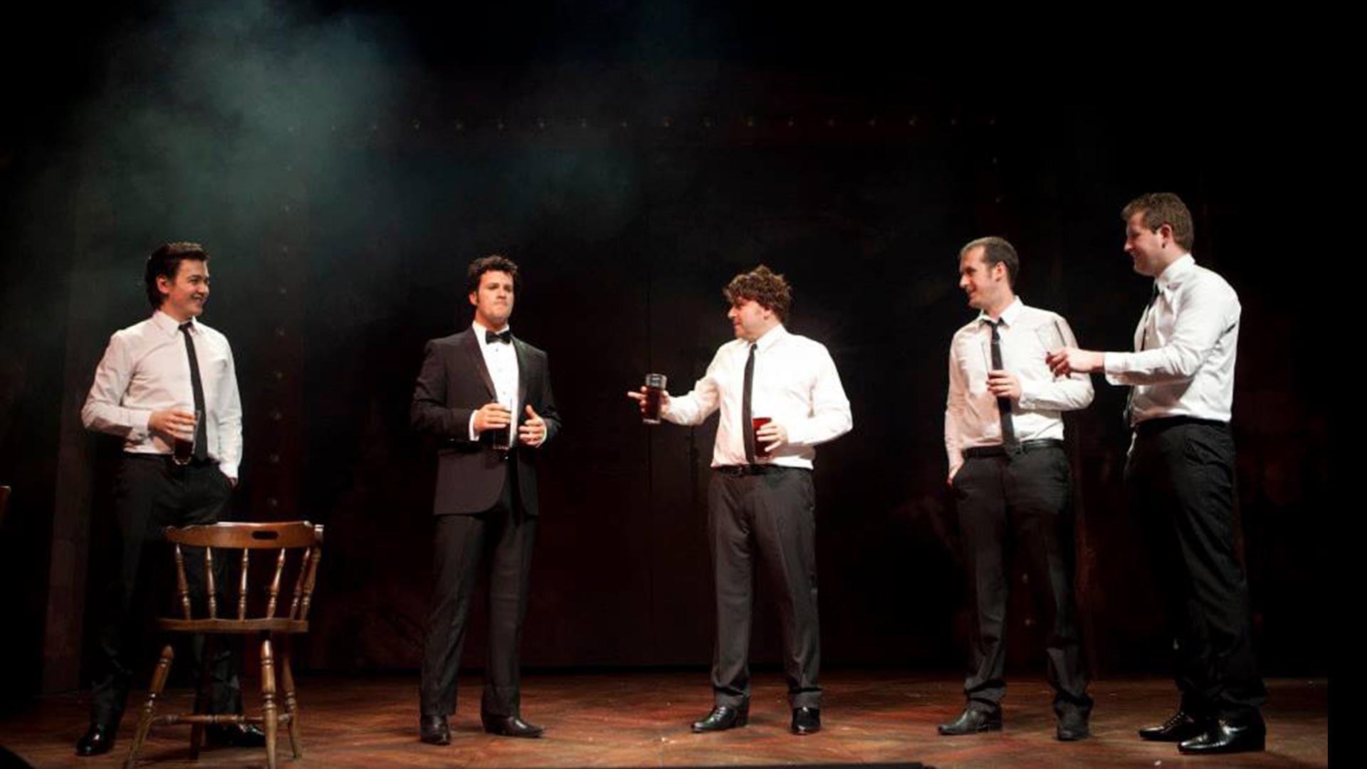 Five people standing holding drinks in a pub scene