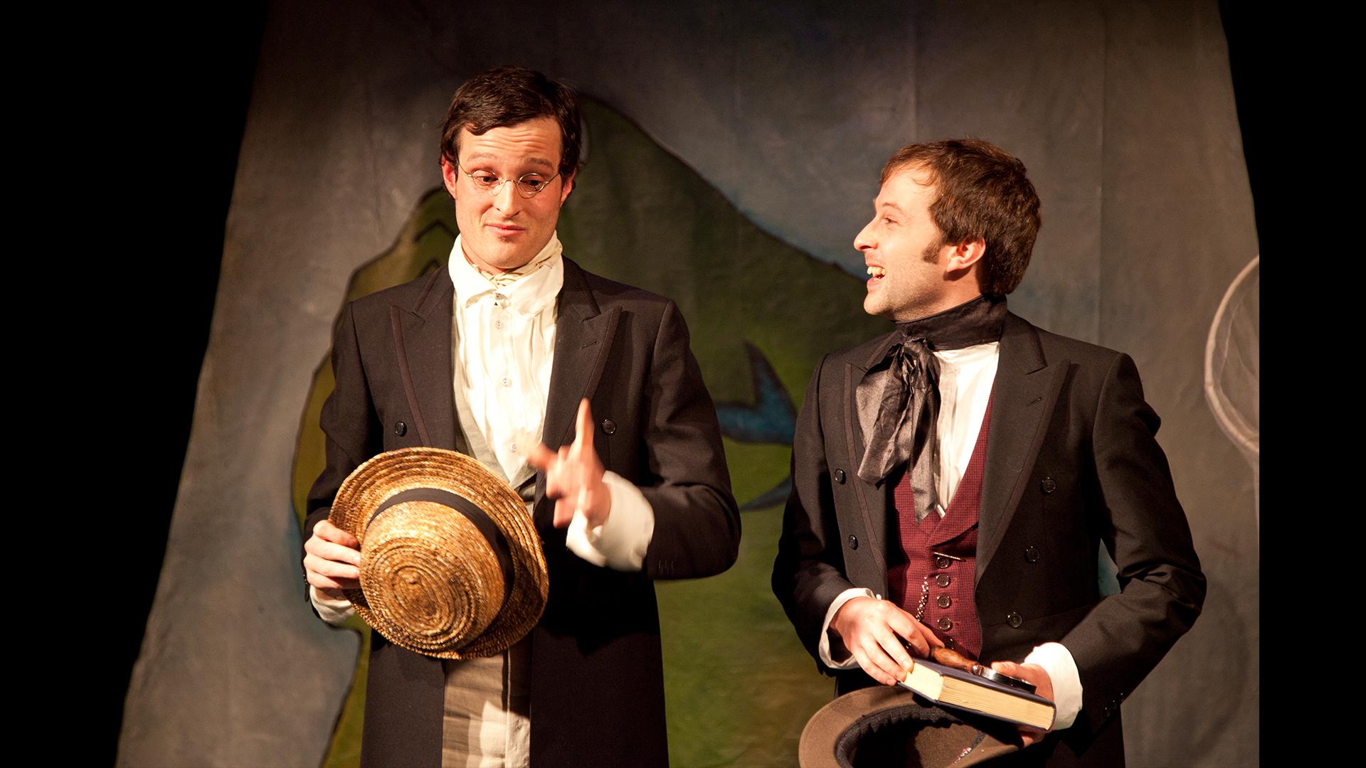 Two actors dressed as Victoria explorers Wallace and Bates. One holding a straw hat, the other a book.