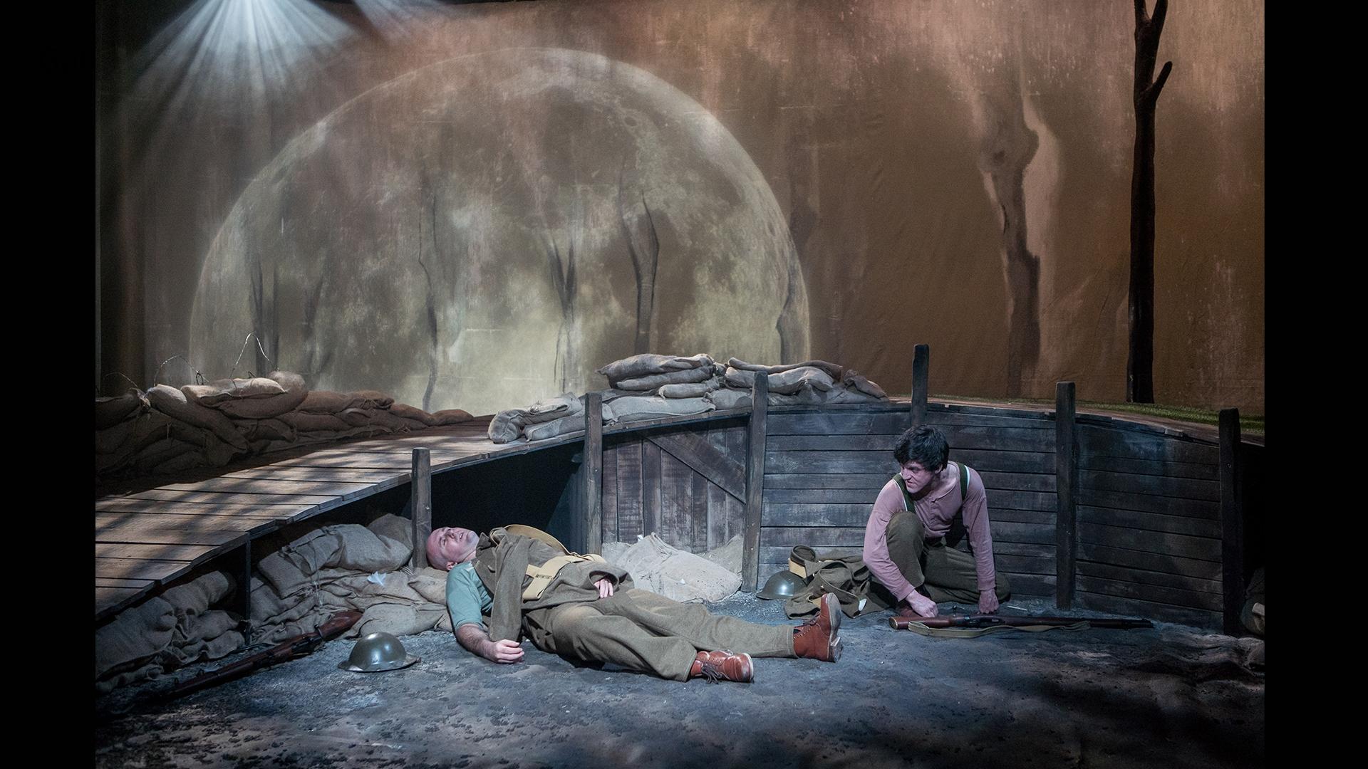 Two soldiers in a World War 1 trench, one lying injured