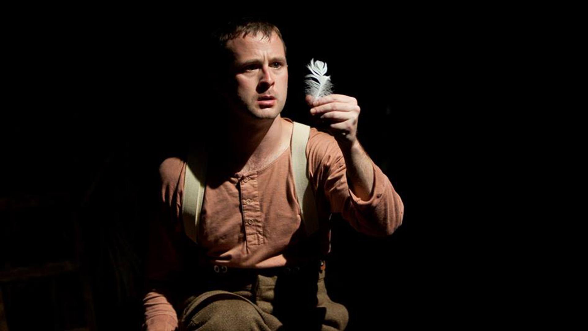 Young soldier looking at a white feather he is holding.