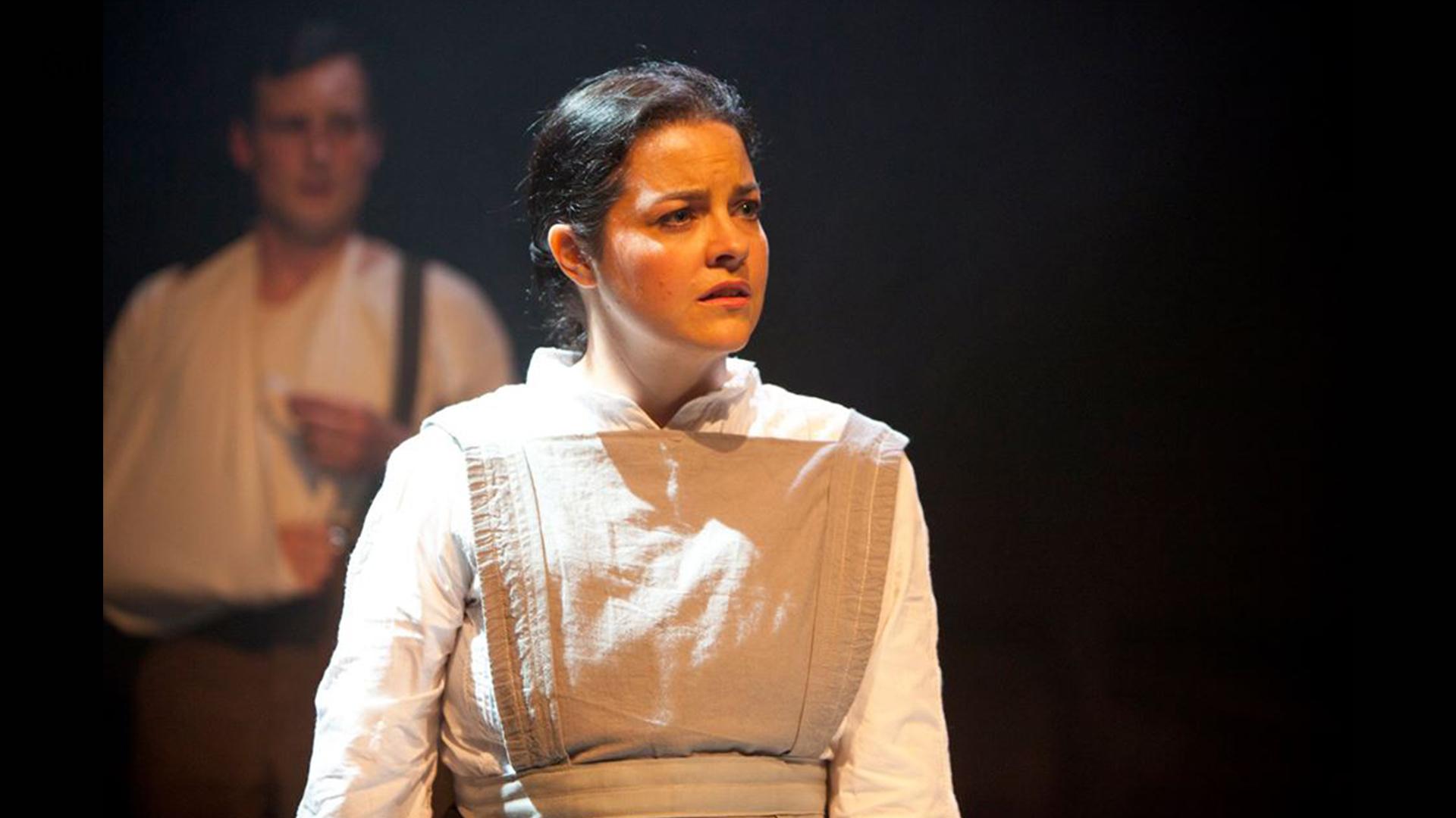 A young woman wearing a white blouse and beige pinafore 