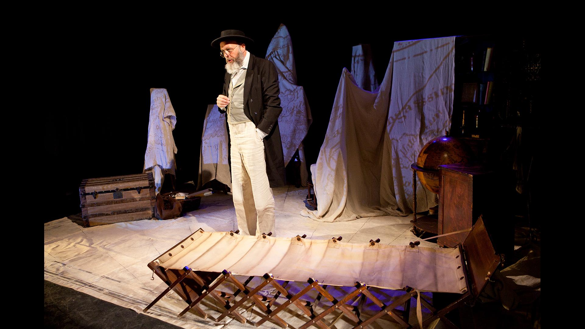 A man dressed in Victorian clothing standing by a camp bed