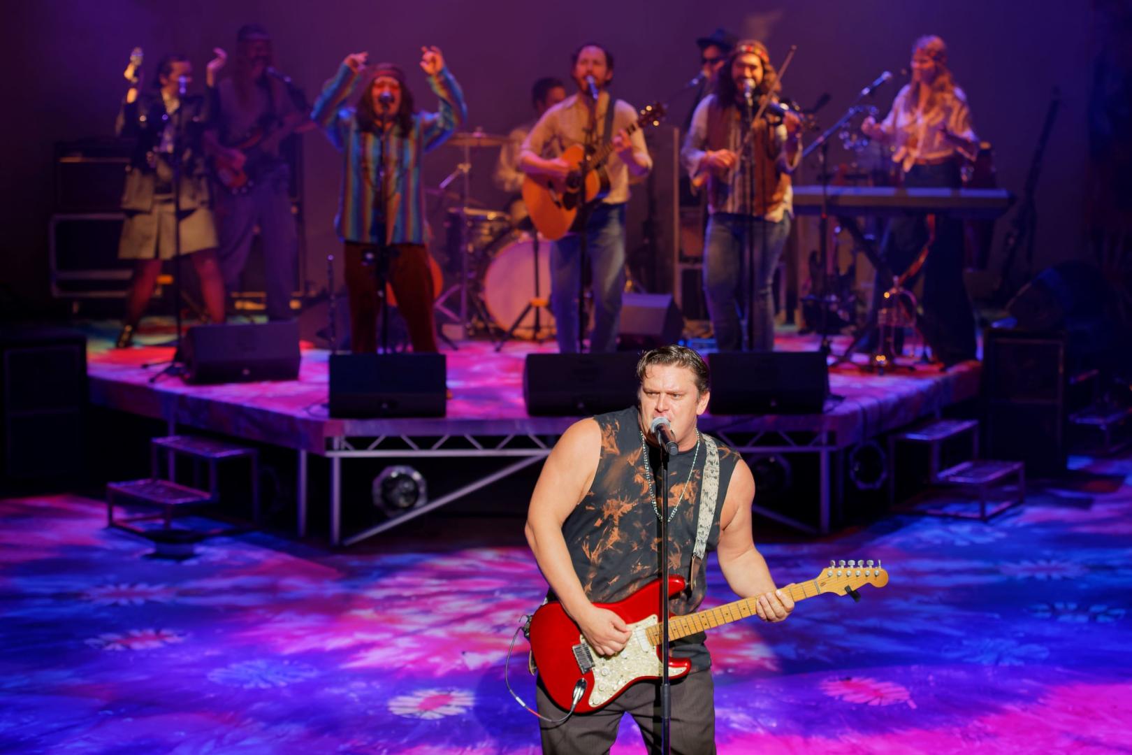 Man playing guitar with band stood behind