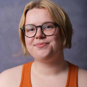 White person with short blonde hair just past their ears and round glasses