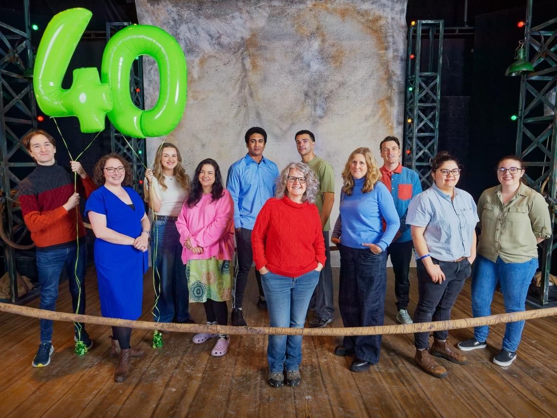 Staff Theatr na nÓg a chwmni The Fight yn sefyll ar lwyfan yn dal dau falŵn werdd siâp 40